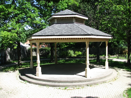 gazebo in sunlight with a shaded interior and green trees surrounding it