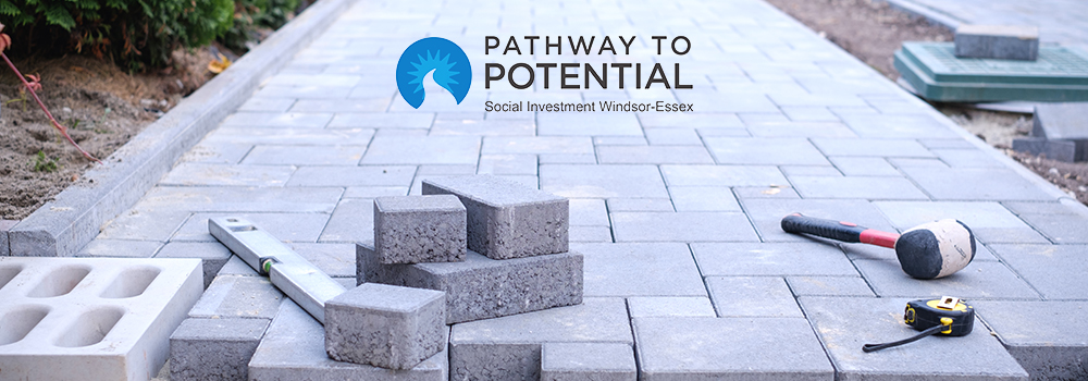 A brick path under construction, tools, and logo for Pathway to Potential Social Investment Windsor-Essex
