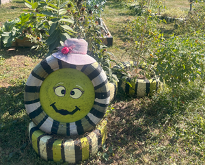 Clickable thumbnail, image of a painted smiley face on a tire that outlines a whole community garden