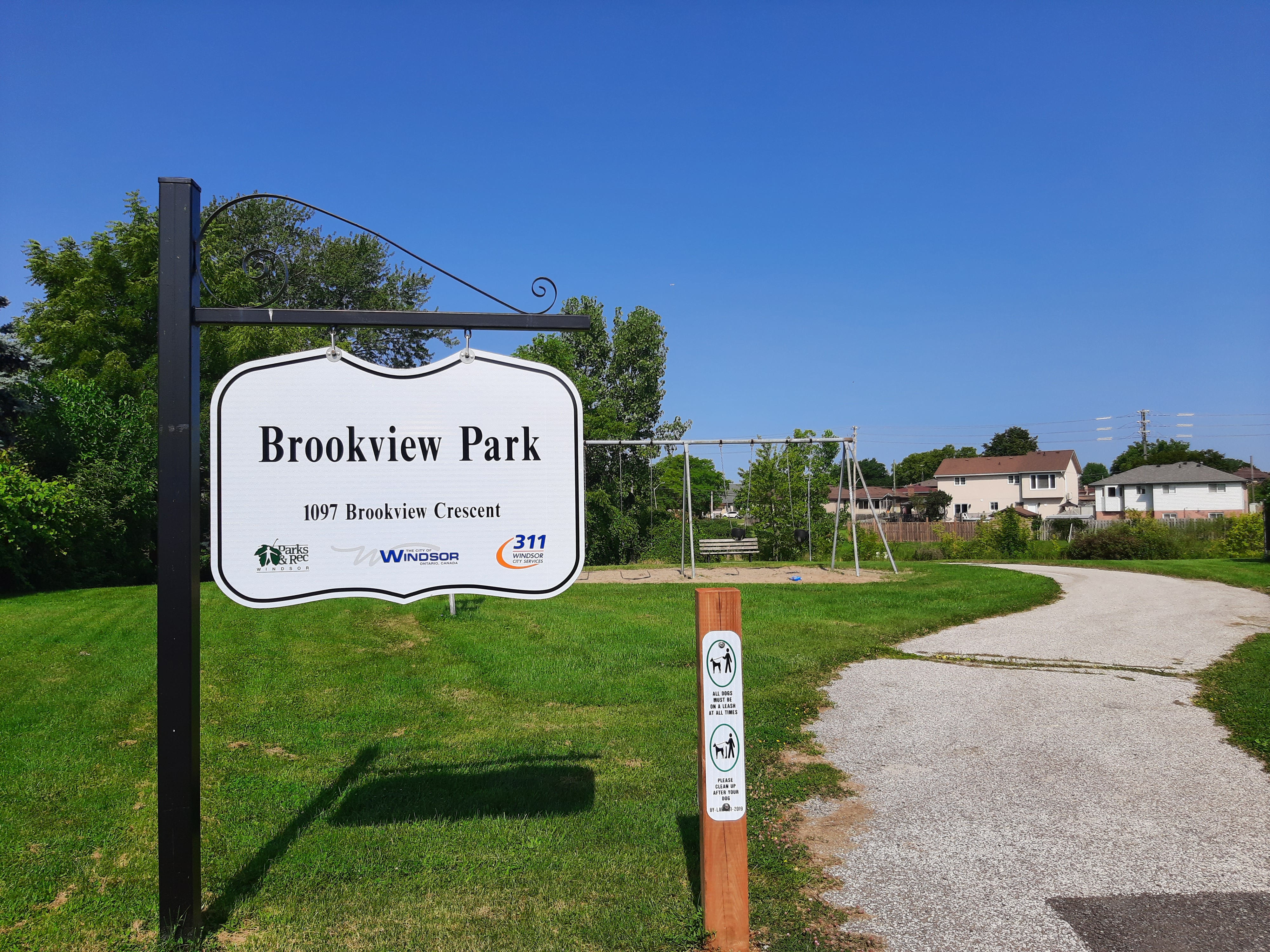 Brookview Park Sign for Brookview Park with swings and paved trail in background